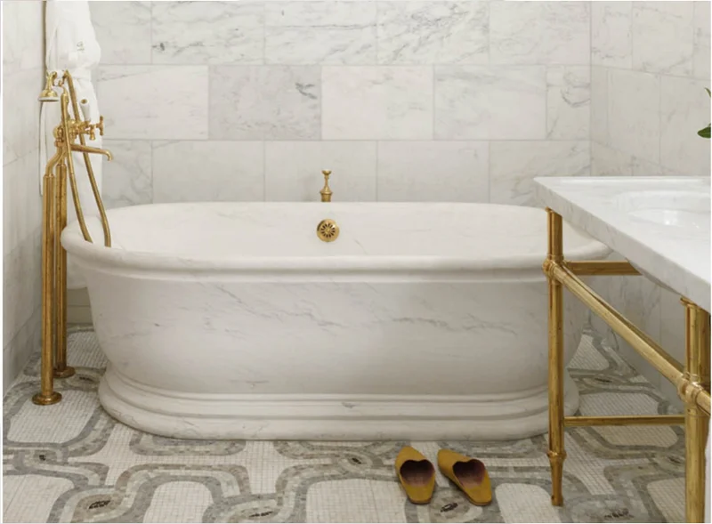 Luxury marble bathroom with hand-carved bathtub and gold fixtures at The Greenwich Hotel, NYC